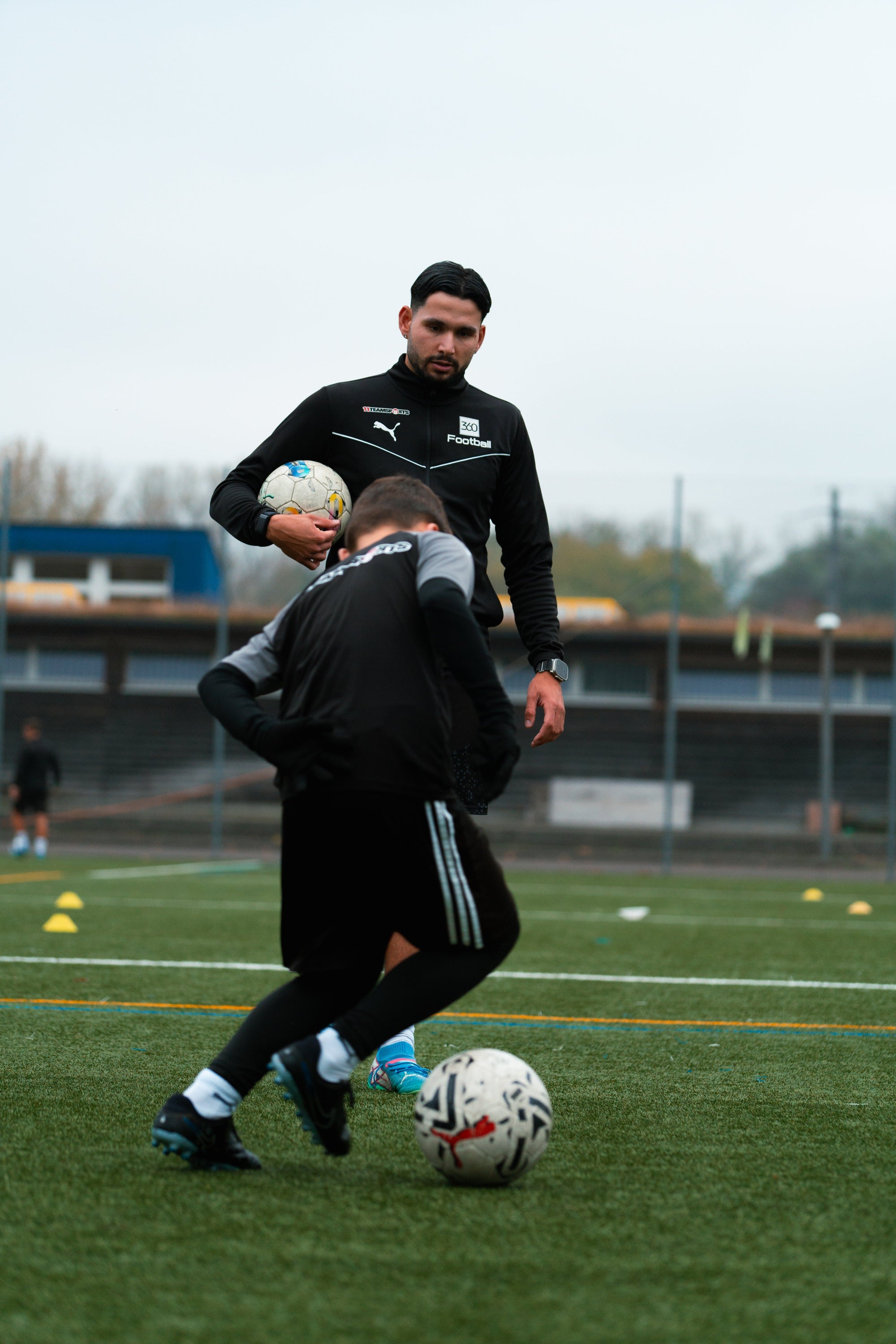 Fussballtrainer beobachtet einen jungen Spieler beim Dribbeltraining auf dem Platz.